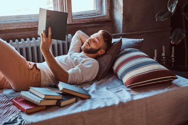 Onun yatakta kitap okuyarak bir yakışıklı öğrenci adam portresi. Eğitim kavramı.
