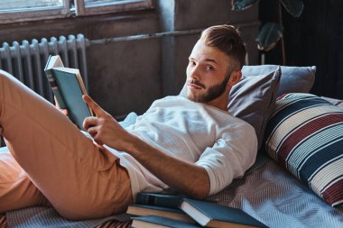 Kameraya bakarak onun yatakta bir kitap bir yakışıklı öğrenci adam portresi tutar.