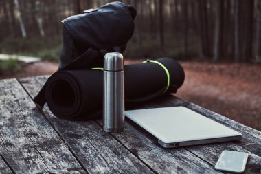 Seyahat kavramı. Sırt çantası, turist mat, dizüstü bilgisayar, akıllı telefon ve Termos şişe güzel orman içinde ahşap bir masa üzerinde.
