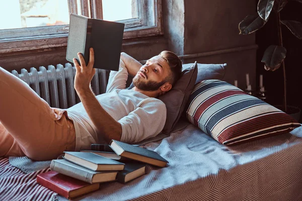 Portret van een man van de knappe student lezen van een boek in zijn bed. Onderwijs concept. — Stockfoto