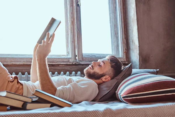 Retrato de un estudiante guapo leyendo un libro en su cama. Concepto educativo . — Foto de Stock