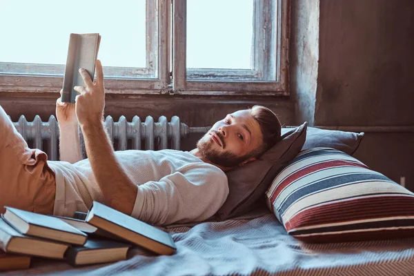 Portret van een man van de knappe student heeft een boek in zijn bed, camera kijken. — Stockfoto