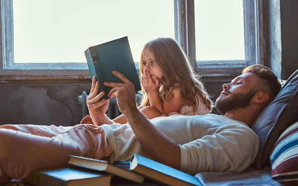 Bonito jovem pai lendo livro de histórias sua filhinha na cama . — Fotografia de Stock