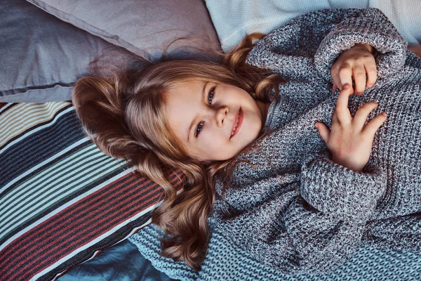 Retrato de cerca de una niña en suéter caliente acostada en la cama . — Foto de Stock