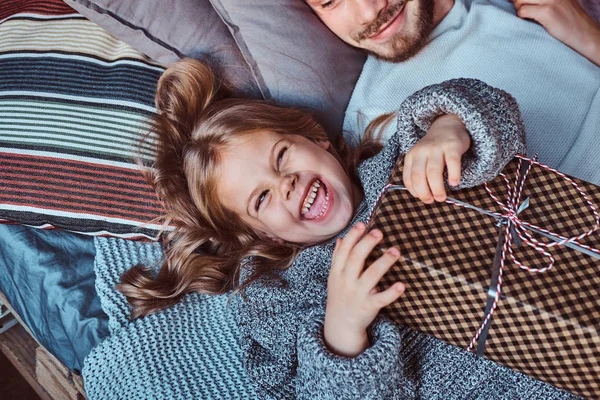 Közelkép portréja a boldog kicsi lány meleg pulóver tart ajándékok ágyon fekve. — Stock Fotó