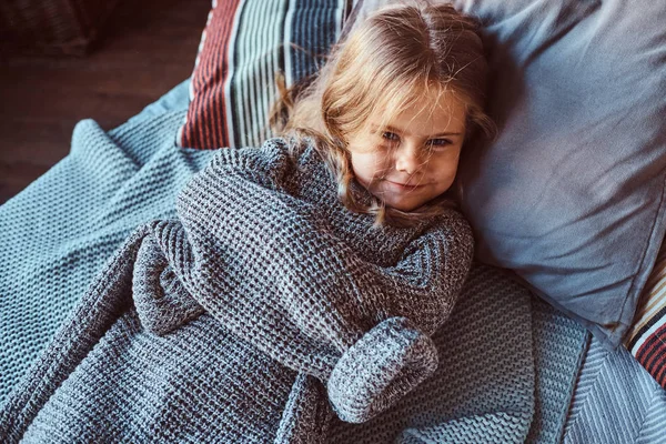 Retrato de cerca de una niña en suéter caliente acostada en la cama . — Foto de Stock