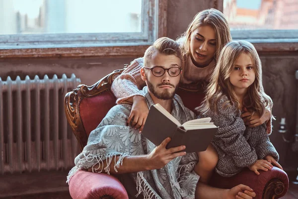 Ensemble, en famille. Maman, papa et fille lisant le livre d'histoires ensemble assis sur le canapé. Concept de famille et de parentalité . — Photo
