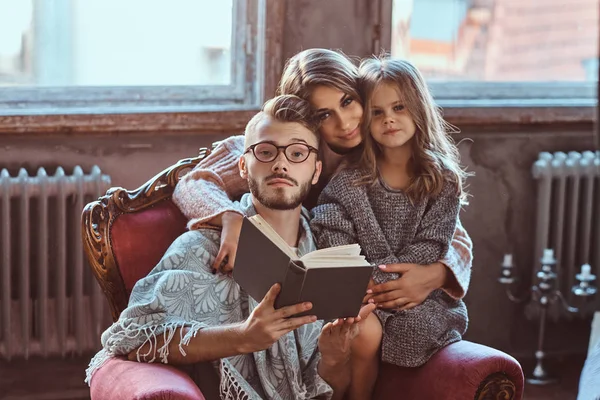 Reunião familiar. Mãe, pai e filha lendo livro de histórias juntos sentados no sofá. Conceito de família e paternidade . — Fotografia de Stock