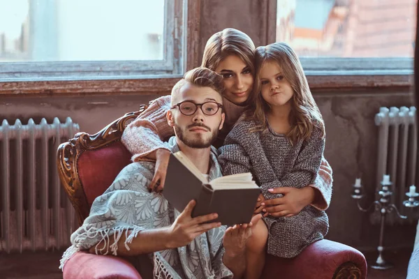 Family togetherness. Mom, dad and daughter reading story book together sitting on the couch. Family and Parenthood Concept. — Stock Photo, Image