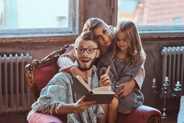 Reunião familiar. Mãe, pai e filha lendo livro de histórias juntos sentados no sofá. Conceito de família e paternidade . — Fotografia de Stock