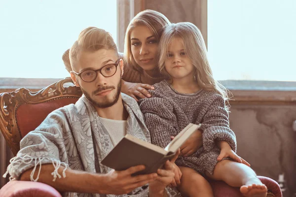 Family togetherness. Mom, dad and daughter reading story book together sitting on the couch. Family and Parenthood Concept. — Stock Photo, Image