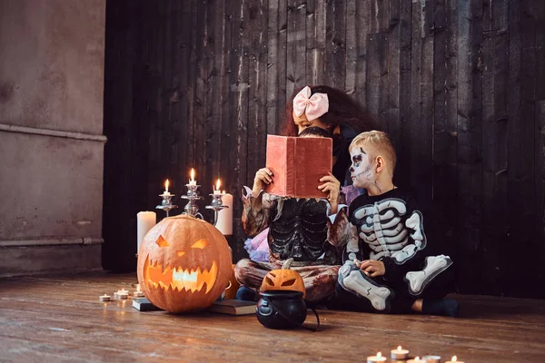 Grupo de crianças multirraciais bonitos em trajes assustadores lendo histórias de terror em uma casa velha, durante a festa de Halloween . — Fotografia de Stock