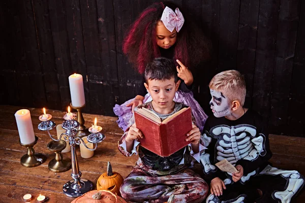 Grupo de lindos niños multirraciales en trajes de miedo leyendo historias de terror en una casa vieja, durante la fiesta de Halloween . —  Fotos de Stock