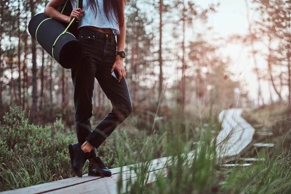 Beskuren bild av en turist tjej innehar en smartphone när du står på en trä gångstig i vacker skog. — Stockfoto