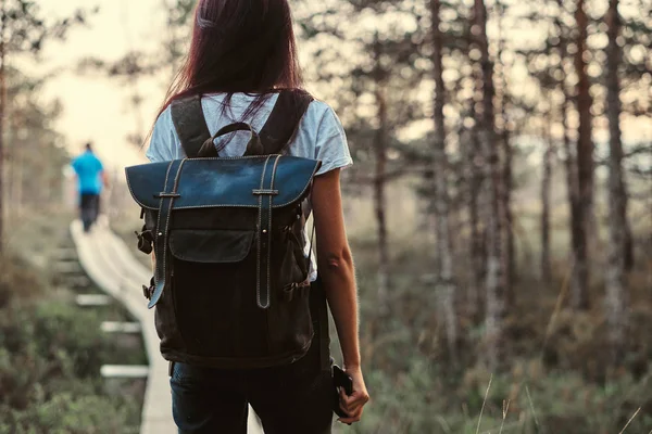 Baksidan på en turist tjej med ryggsäck promenad på en trä gångstig i vacker skog. — Stockfoto