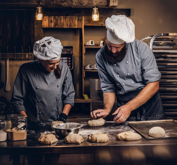 Chef teaching his assistant to bake the bread in a bakery.