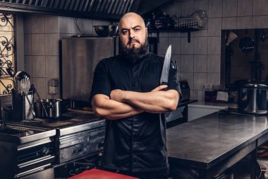 Siyah üniformalı sakallı aşçı bıçak ve Çapraz kollar ile ayakta tutan mutfakta.