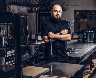 Siyah üniformalı sakallı aşçı bıçak ve Çapraz kollar ile ayakta tutan mutfakta.