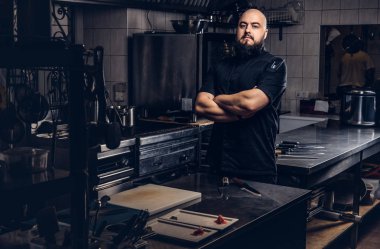Mutfakta çapraz kolları olan siyah üniforma ayakta acımasız sakallı Şef aşçı.