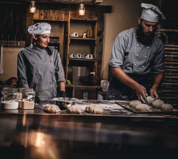 Koch lehrt seine Assistentin, das Brot in einer Bäckerei zu backen. — Stockfoto