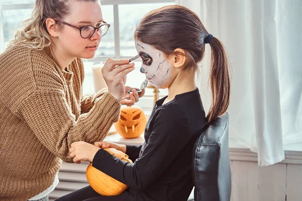 Mamma måla dotter ansikte för Halloween-fest. — Stockfoto