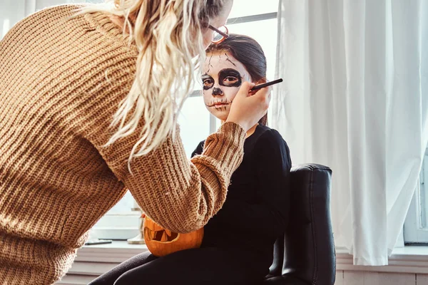 Mamma måla dotter ansikte för Halloween-fest. — Stockfoto