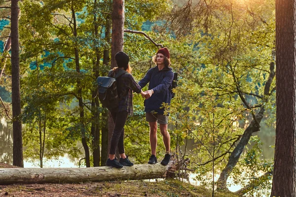 Güzel bir ormandaki bir ağaç gövdesi üzerinde günbatımında ayakta el ele tutuşarak genç hippi çift. Seyahat, turizm ve zammı kavramı. — Stok fotoğraf