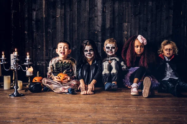 Halloweenfest med gruppen barn som sitter ihop på ett trägolv i ett gammalt hus. Halloween-konceptet. — Stockfoto