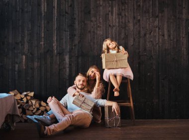 Aile kavramı. Anne, baba ve kızı ile birlikte hediye ahşap duvar karşı boş odada. 