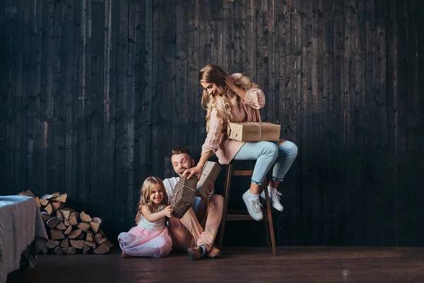 Familjen koncept. Mamma, Pappa och dotter tillsammans med gåvor i tomt rum mot väggens trä. — Stockfoto