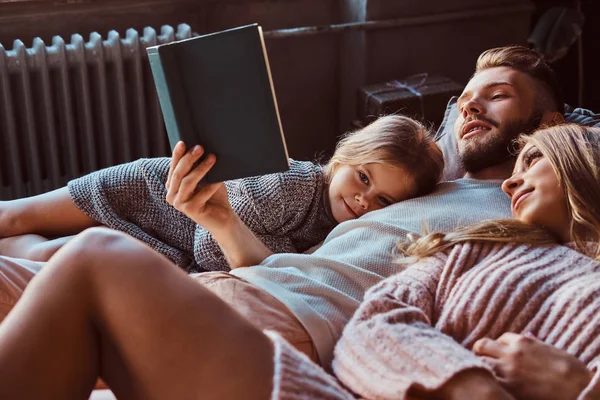 Mãe, pai e filha lendo o livro de histórias juntos enquanto estavam deitados na cama . — Fotografia de Stock