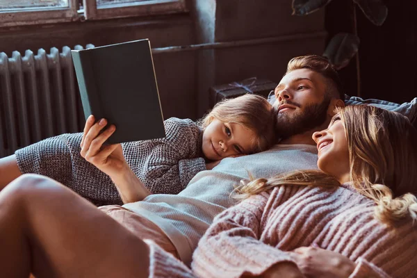 ママ、パパ、娘読む童話のベッドの上に横たわっている間一緒に. — ストック写真