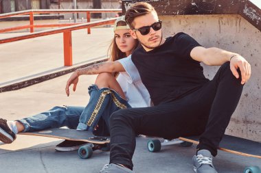 Genç patenciler birlikte güneşli günde kaykaylar skatepark, üzerinde otururken sarılma şık giyimli iki.