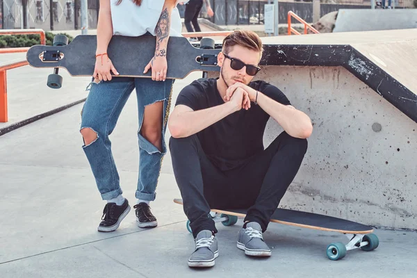一个时髦的时髦家伙坐在一个长板在 skatepark 的肖像. — 图库照片
