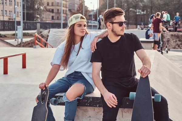 Joven pareja elegante de patinadores vestidos de moda que se relajan en un skatepark . —  Fotos de Stock