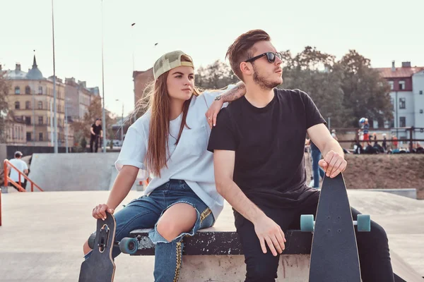 Jovem casal elegante de uma moda vestidos patinadores relaxando em um parque de skate . — Fotografia de Stock