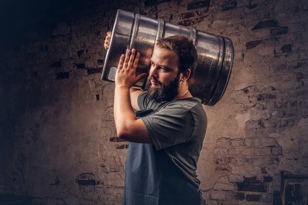 Cervecero en delantal sostiene barril con cerveza artesanal en fábrica de cerveza . — Foto de Stock