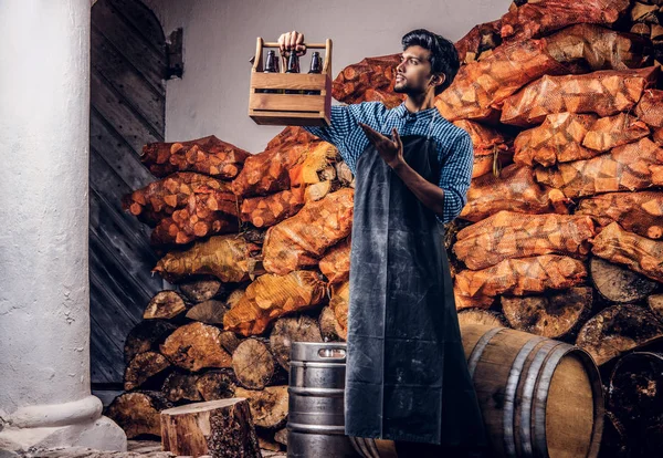 Cervecero profesional en delantal mostrando caja de madera con los productos de su cervecería . — Foto de Stock