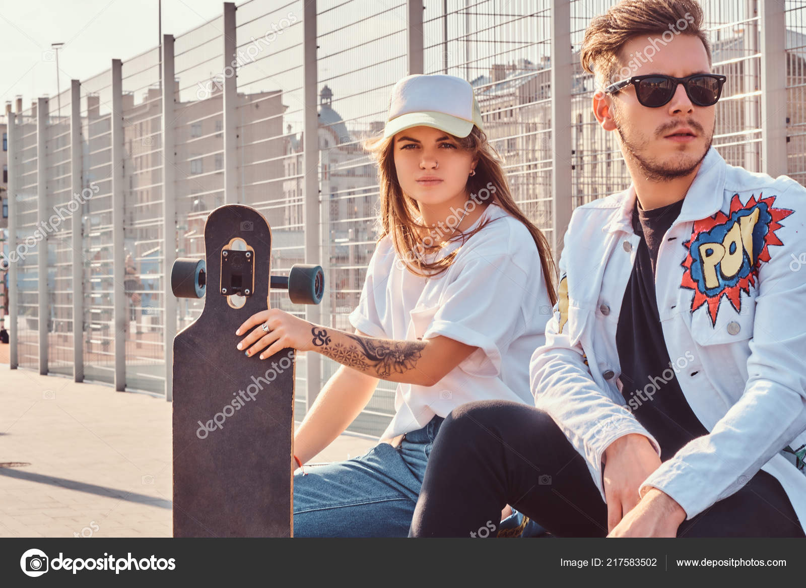 Atractive Couple Of Trendy Dressed Young Hipsters With Skateboards