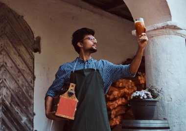 Uzman brewer önlük ayakta açık havada bira fabrikası'nda demlenmiş içecek kalitesini kontrol.