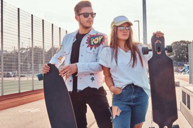 Atractive çift şık giyimli genç hipsters kaykaylar şehir spor güneşli günde kompleksi ile poz