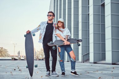 Kaykaylar gökdelen yakınındaki ile poz trendy elbise giymiş çekici genç çift.