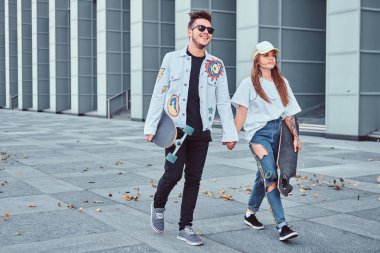 Mutlu genç çift el ve rüzgarlı havalarda modern sokakta kaykay ile birlikte yürüyüş tutun.