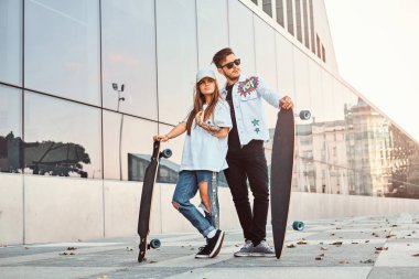 Kaykaylar gökdelen yakınındaki ile poz trendy elbise giymiş çekici genç çift.