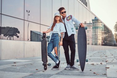 Kaykaylar gökdelen yakınındaki ile poz trendy elbise giymiş çekici genç çift.