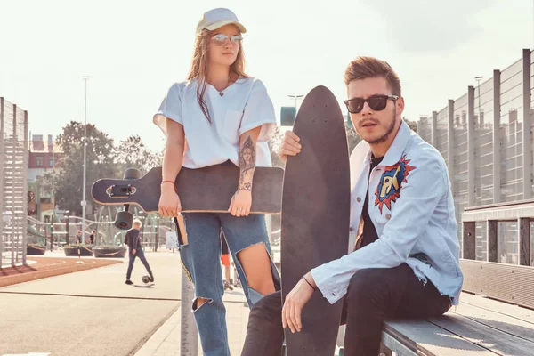 Närbild porträtt av unga trendiga klädd hipster par med skateboards som poserar på city sport komplex solig dag — Stockfoto