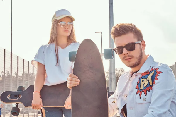 Närbild porträtt av unga trendiga klädd hipster par med skateboards som poserar på city sport komplex solig dag — Stockfoto