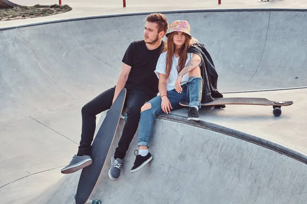 Fiatal csípő pár divatos öltözött pihentető együtt egy skatepark a gördeszka, egy napsütéses napon. — Stock Fotó