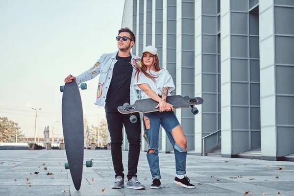 Attraktives junges Paar in trendiger Kleidung posiert mit Skateboards in der Nähe von Wolkenkratzer. — Stockfoto