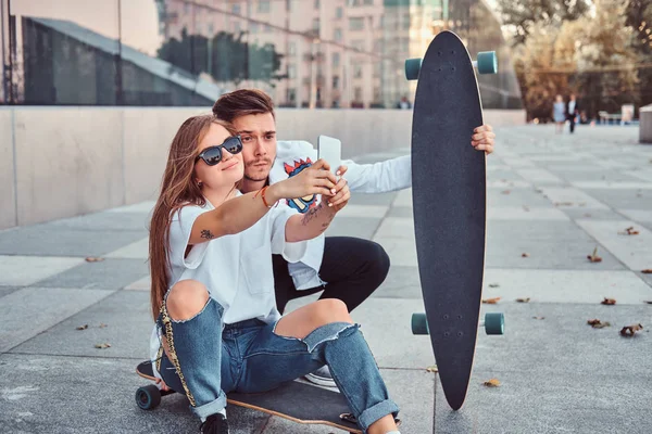 Retrato de pareja joven vestida con ropa de moda divirtiéndose mientras hace una selfie juntos al aire libre . — Foto de Stock